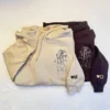 Sand hoodie over a dark brown one, both with a stitched couple outline and heart initials M and D on the sleeves