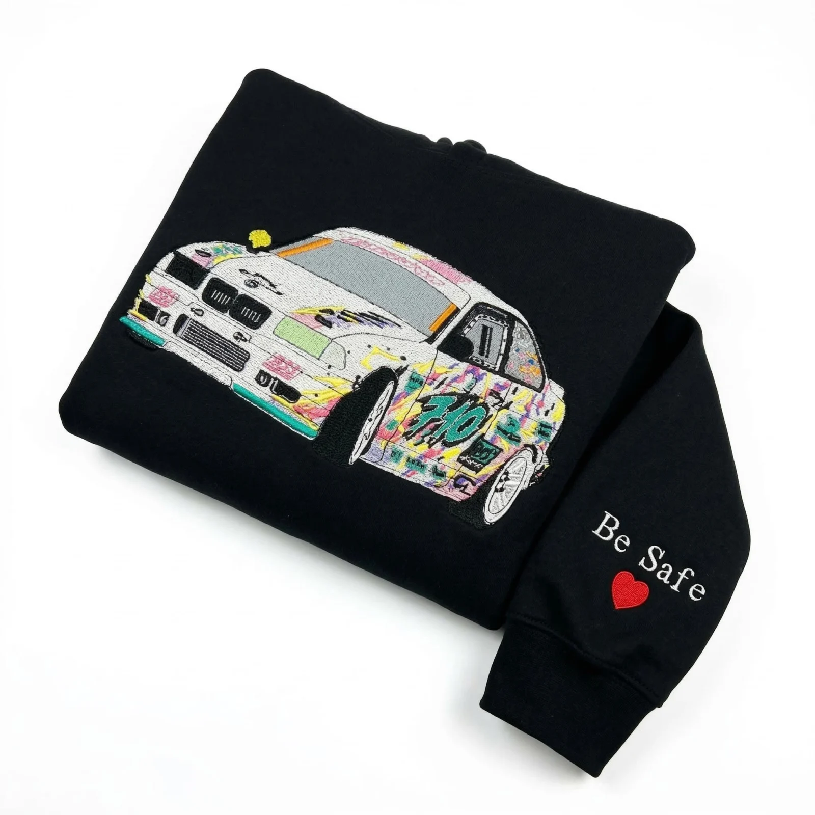 Folded black hoodie with a detailed white drift car in pink, yellow and teal graffiti livery and a Be Safe sleeve