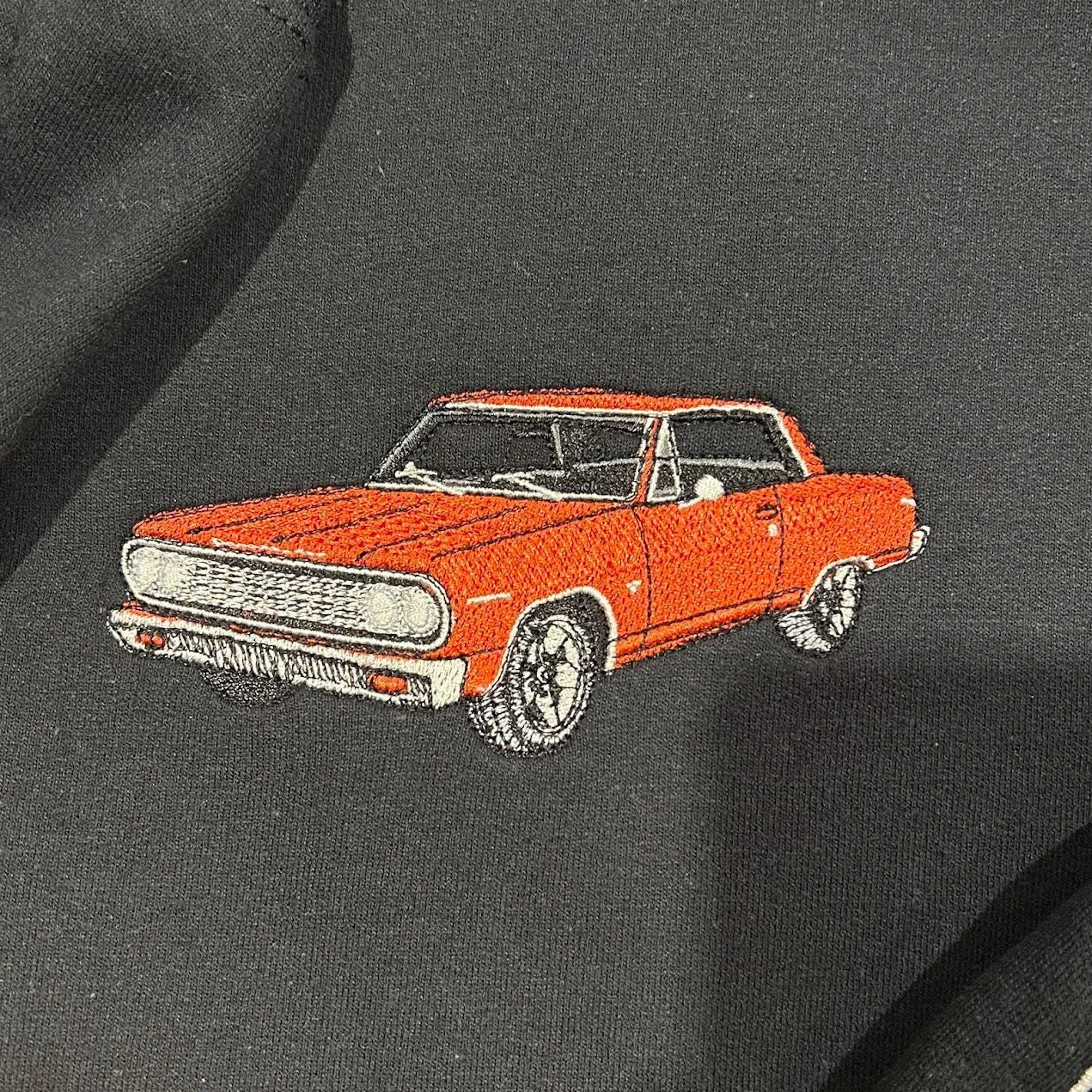 Close-up of an embroidered orange classic coupe with chrome trim and black tyres on black fleece