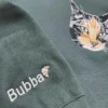 Forest green sweatshirt with an embroidered calico cat face on the chest and the name Bubba with a croissant on the sleeve