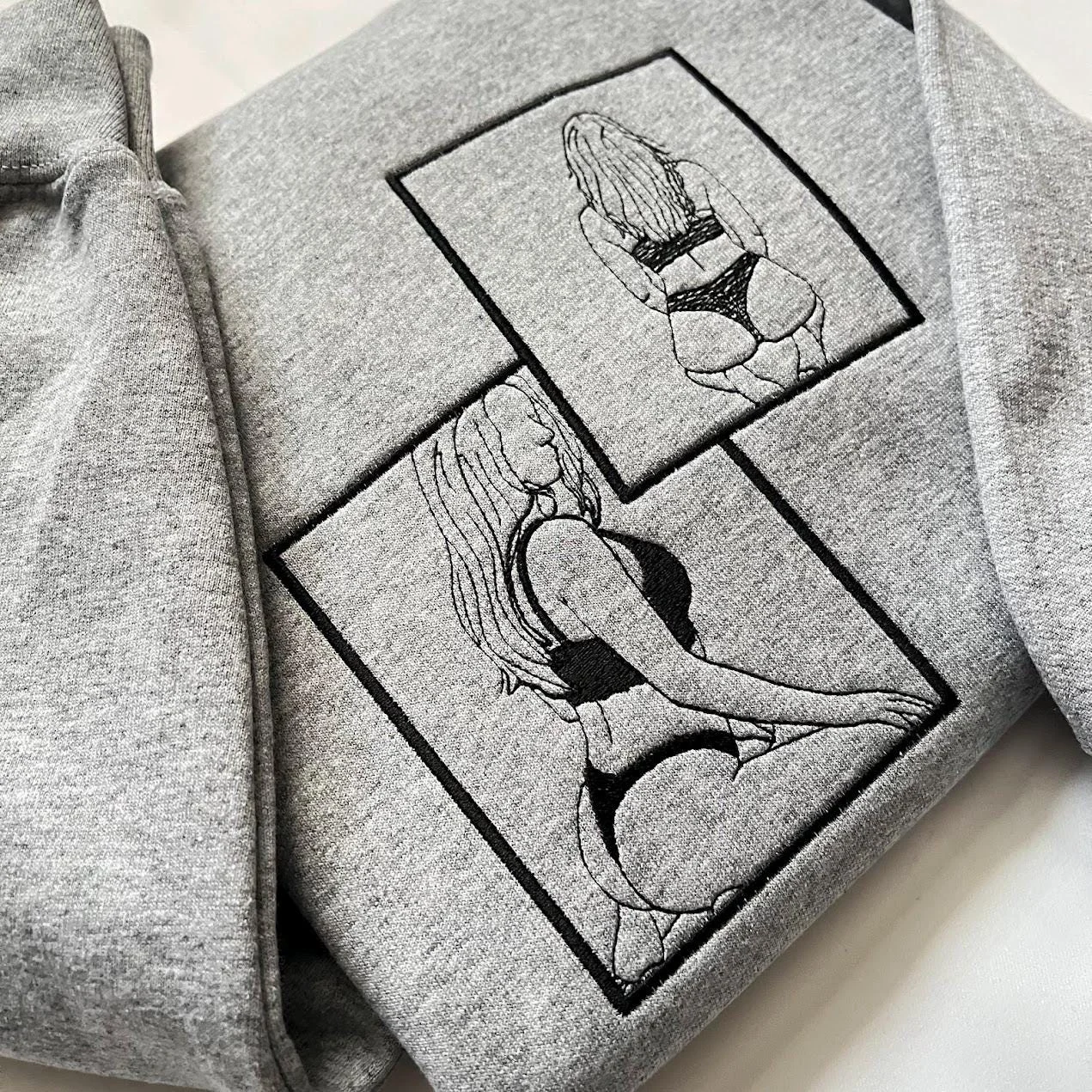 Grey sweatshirt angled to show two overlapping framed outline portraits of a woman from behind in black thread