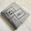 Grey sweatshirt folded at an angle with two framed outline portraits embroidered in black thread