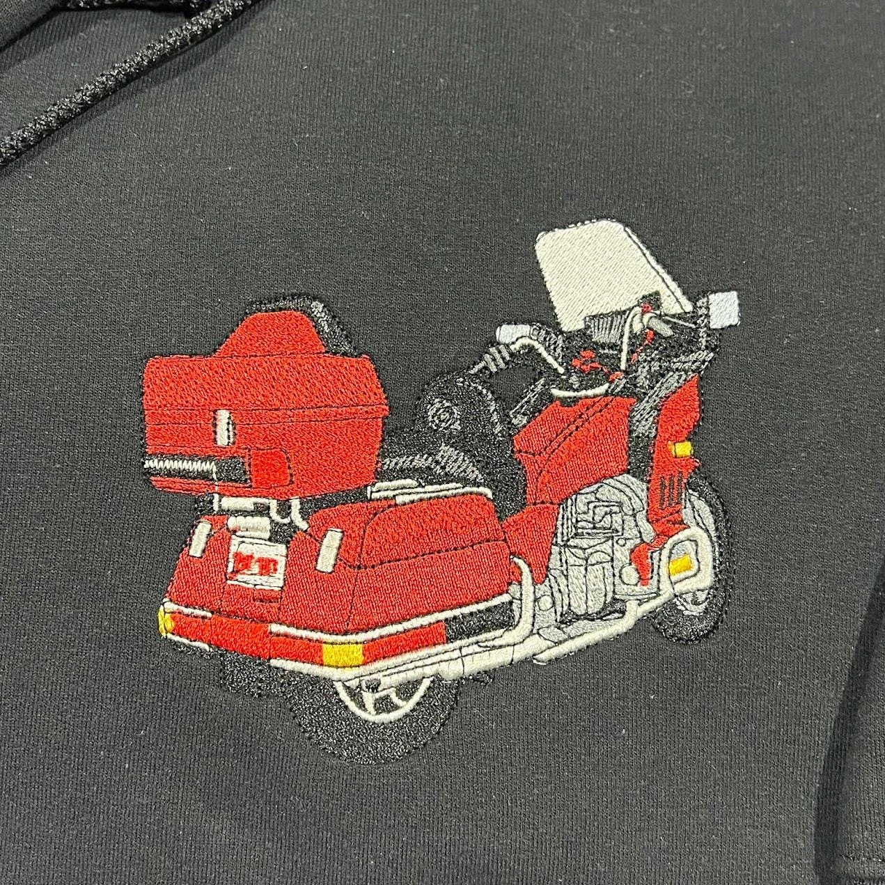Close-up of a thread-painted red touring motorcycle with top case and windshield on black fleece