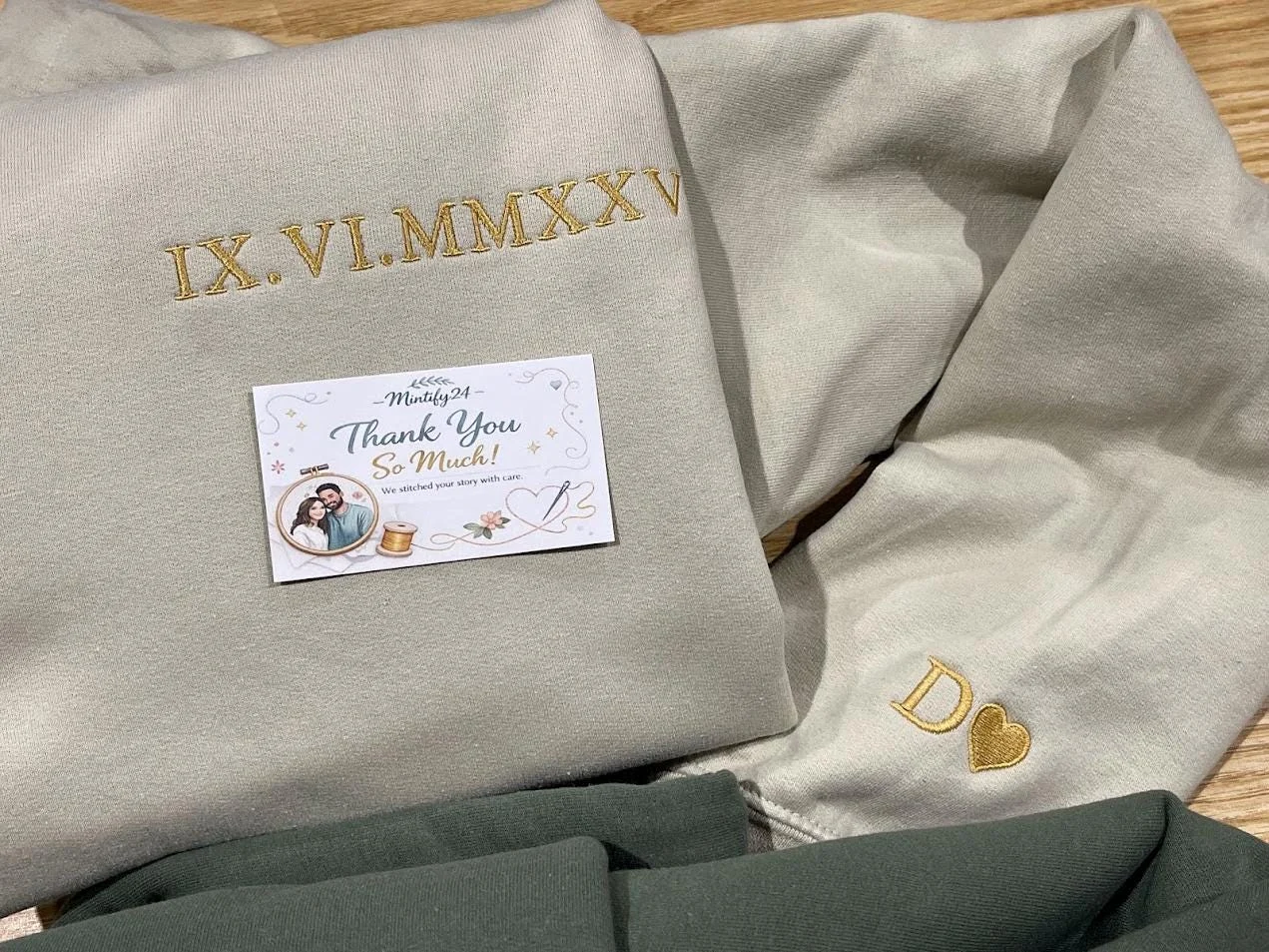 Close-up of IX.VI.MMXXV in gold Roman numerals and a gold D with a heart stitched near a light beige cuff