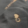 Close-up of copper Roman numerals IX.XXVII.MMXXIV on a dark hoodie, with a heart and the initial C on the cuff