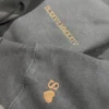 Dark grey hoodie with the date IX.XXVII.MMXXIV stitched in copper thread and an S with a heart on the sleeve cuff