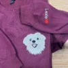 Maroon sweatshirt laid flat with a white dog portrait on the chest and Lexie with a red heart stitched up the sleeve
