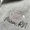 Close-up of embroidered pink heart stethoscope and custom nurse name on quarter zip showing stitch detail