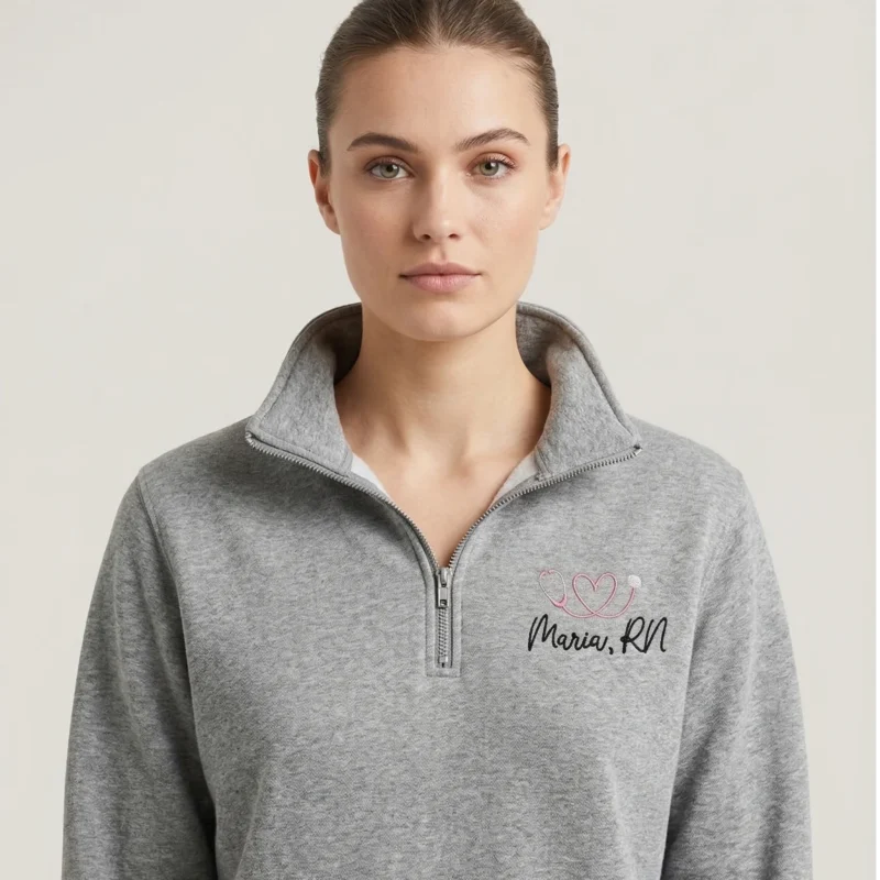 Woman wearing personalized nurse stethoscope embroidered quarter zip in heather grey with pink embroidery