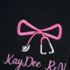 Close-up of embroidered pink bow with white stethoscope ends and custom nurse name on black quarter zip
