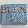 Folded light blue sweatshirt with a large floral nurse embroidery of red and pink roses, daisies and leaves