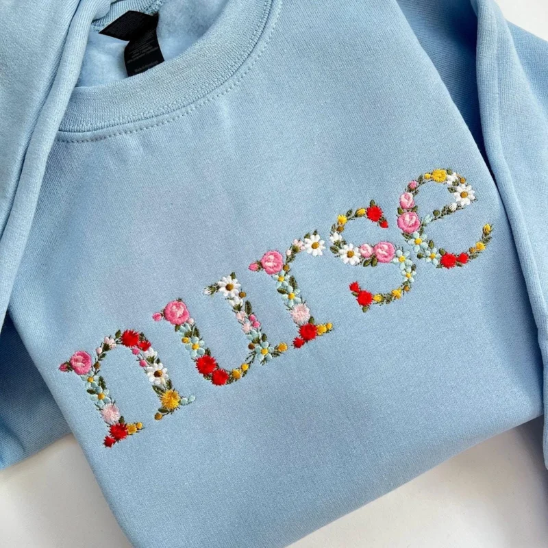 Light blue sweatshirt with the word nurse spelled in lowercase letters made of embroidered roses and daisies