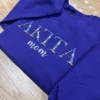 Floral pet name embroidery AKITA with mom in script, stitched on a purple crewneck folded on wood