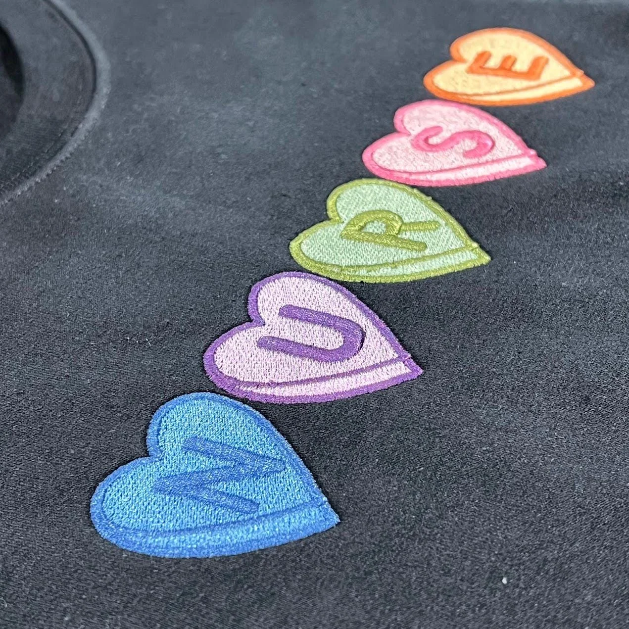 Detail of the stitched candy heart letters N U R S E on a navy sweatshirt, showing the satin fill and outlines