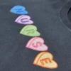 Close-up of five embroidered candy hearts in blue, purple, green, pink and orange, each holding a letter of NURSE