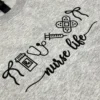 Diagonal view of the nurse life embroidery with stethoscope, syringe, pill bottle and crossed bandage icons in black