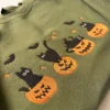 Close-up of four black cats on carved jack-o'-lantern pumpkins embroidered on a military green sweatshirt