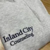 Grey quarter-zip with a counselling practice name embroidered in navy serif lettering on the left chest