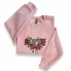 Light pink crewneck laid flat with the colourful Christmas Nurse design and red stethoscope bow on the chest