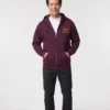 Man standing in a maroon full-zip hoodie and jeans with gold placeholder logo text on the left chest