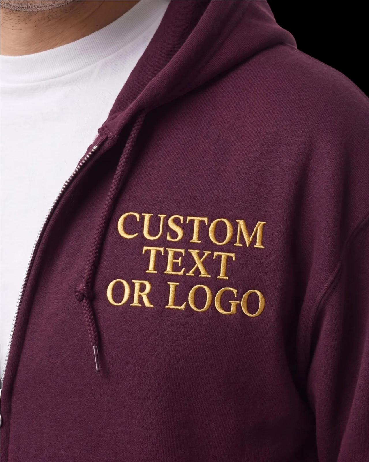 Close-up of a maroon full-zip hoodie with CUSTOM TEXT OR LOGO in gold serif capitals on the left chest