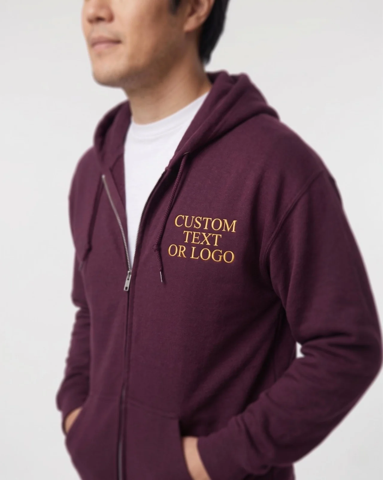 Man wearing a maroon full-zip hoodie with sample gold text CUSTOM TEXT OR LOGO embroidered on the chest