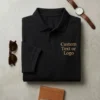 Black polo shirt flat-lay with Custom Text or Logo in gold serif on the left chest, watch and sunglasses beside