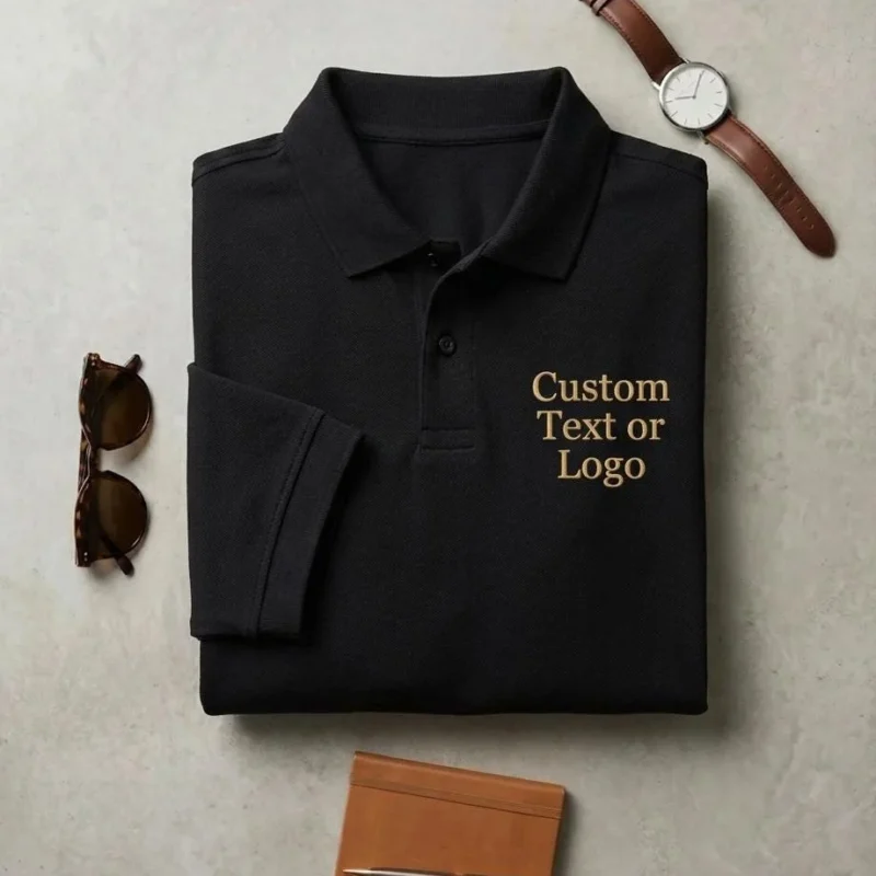 Black polo shirt flat-lay with Custom Text or Logo in gold serif on the left chest, watch and sunglasses beside