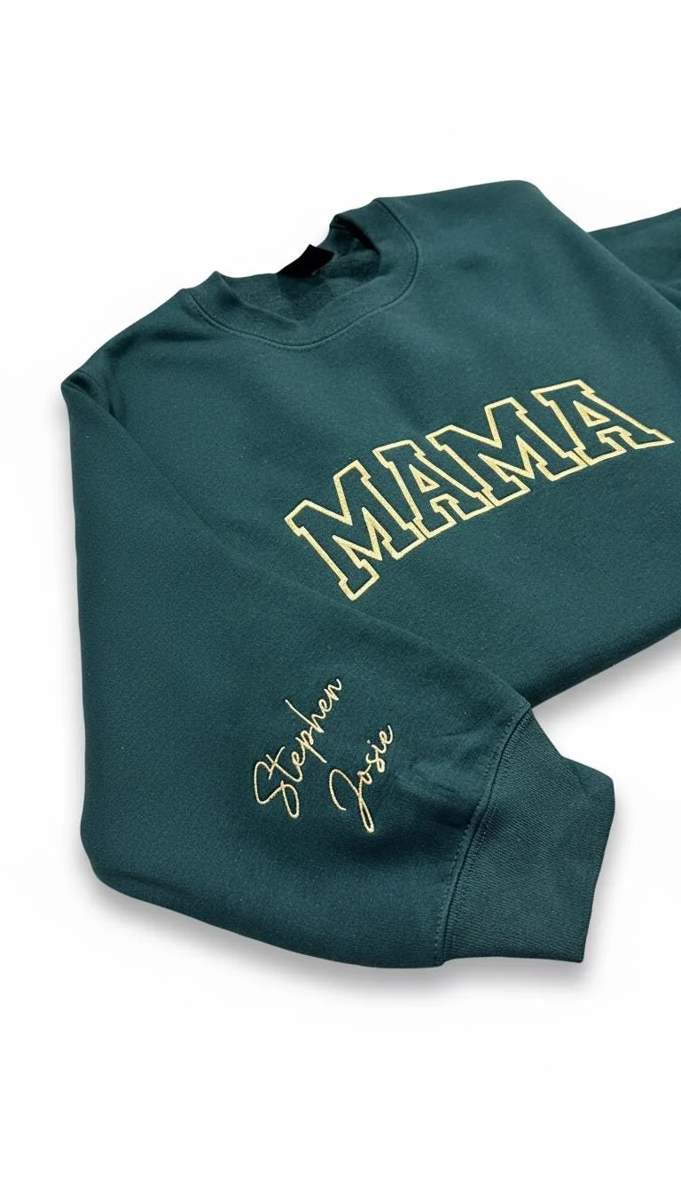 Angled forest green crewneck showing MAMA in cream outlined varsity letters and two names stitched on the cuff