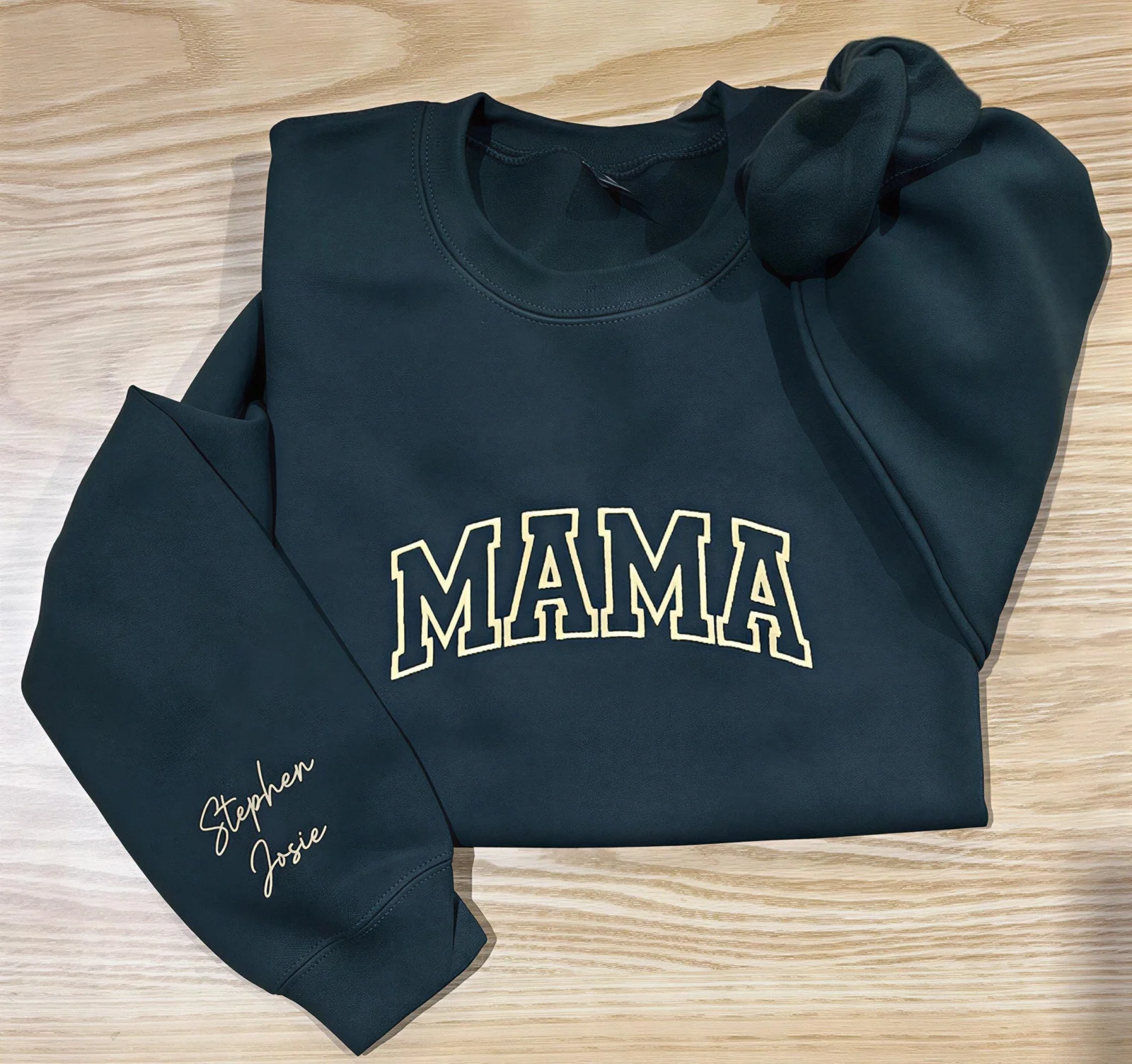 Forest green MAMA sweatshirt on a wooden floor with Stephen and Josie embroidered in cream script on the sleeve