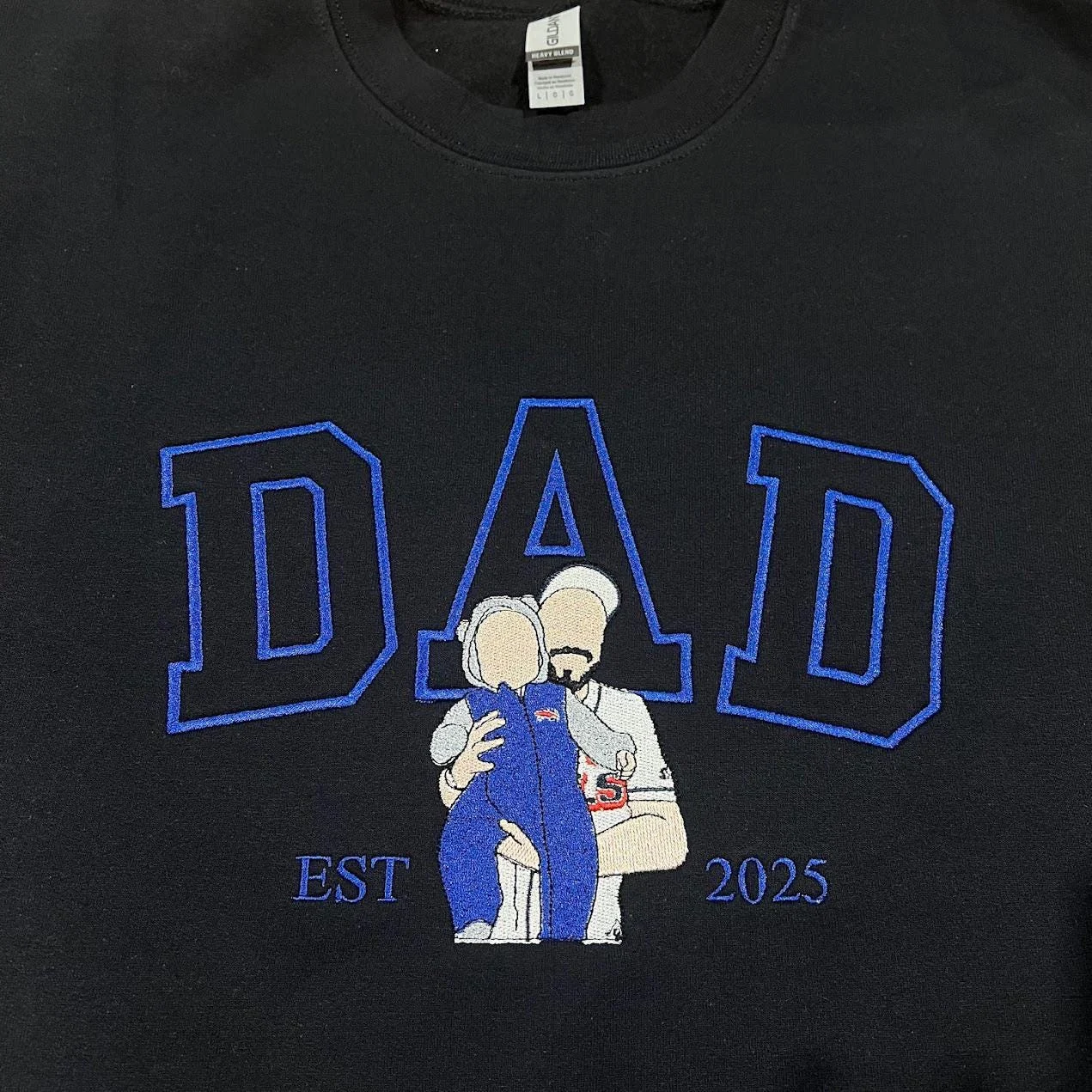 Dad portrait embroidery on a black sweatshirt: royal blue outline DAD and a dad holding a baby in blue, EST 2025