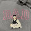 Dad portrait embroidery on a grey sweatshirt: pink outline DAD and a tattooed dad in a cap cradling his baby