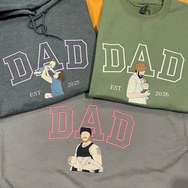 Three embroidered DAD portrait tops in dark grey, military green and grey, each with a dad holding his baby