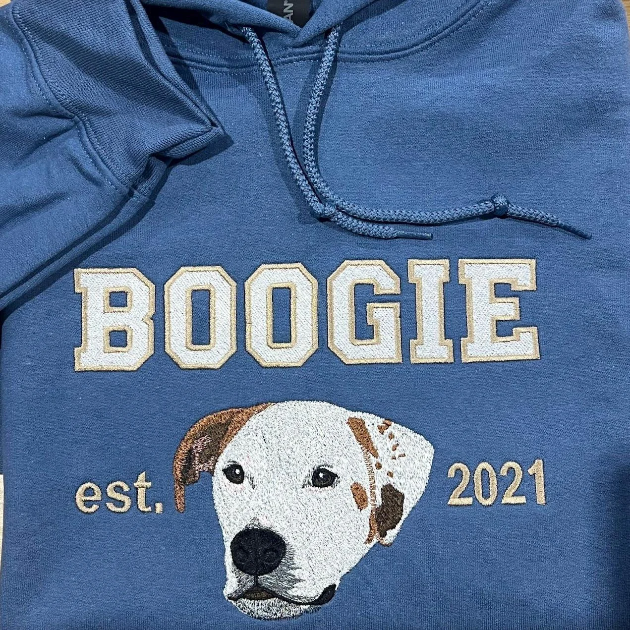 Close-up of a stitched white dog with brown ears under the name BOOGIE, with est. and 2021 on either side
