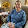 Smiling grandmother in an armchair wearing a blue crewneck with Grandma stitched in white script near the collar
