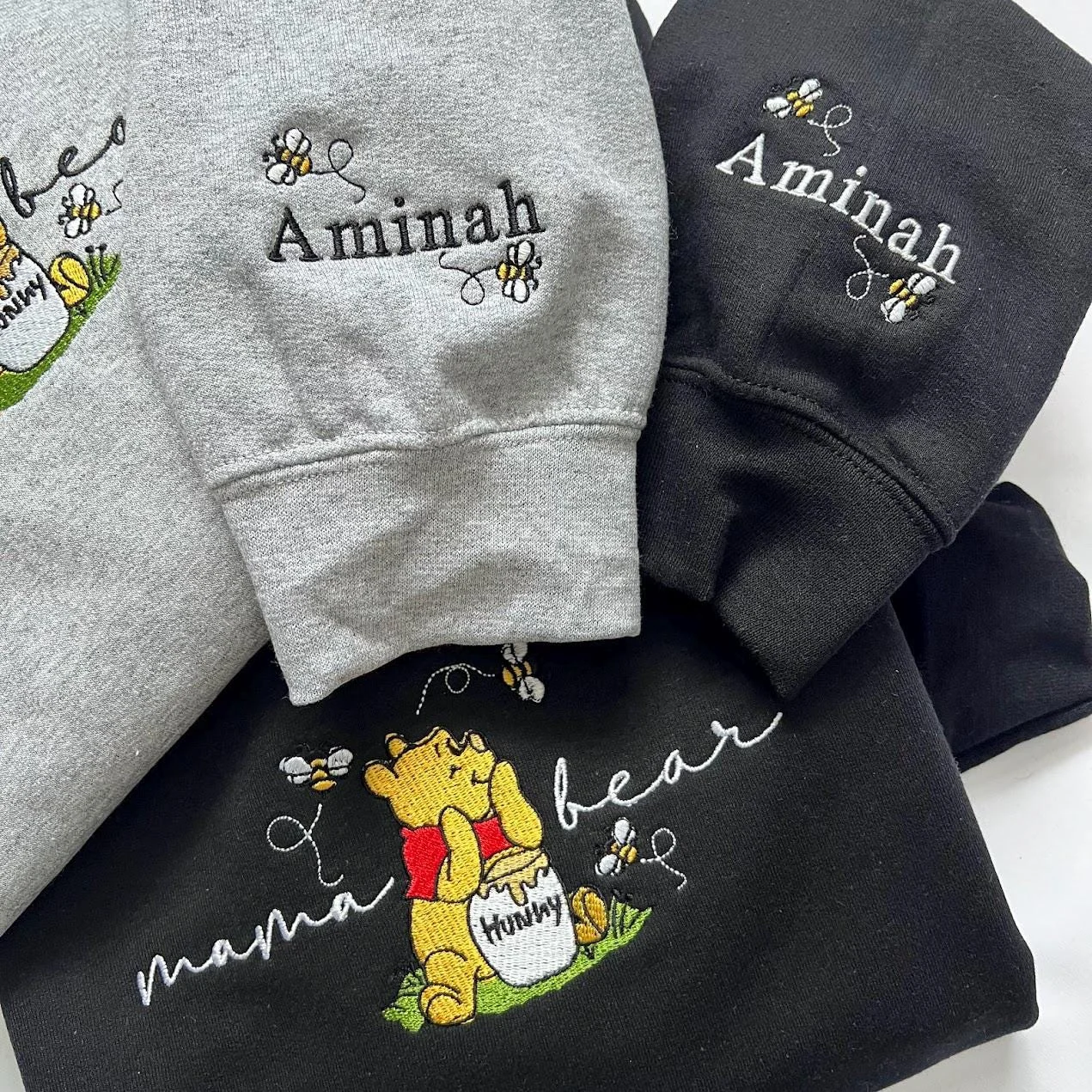 Grey and black sweatshirt sleeves embroidered with the name Aminah and small bees, above the mama bear design
