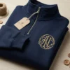 Folded navy quarter-zip with a gold ornate circle monogram embroidered on the left chest, beside a kraft tag