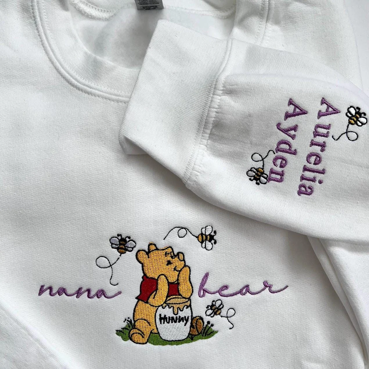 White sweatshirt with nana bear in purple script, the honey pot bear, and Aurelia and Ayden in purple on the sleeve