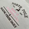 Diagonal close-up of the reindeer bakery sign embroidery in dark brown and pink thread on a sand sweatshirt