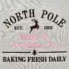 Straight-on close-up of NORTH POLE EST. 1802 with a leaping reindeer above Milk & Cookies Co. in pink