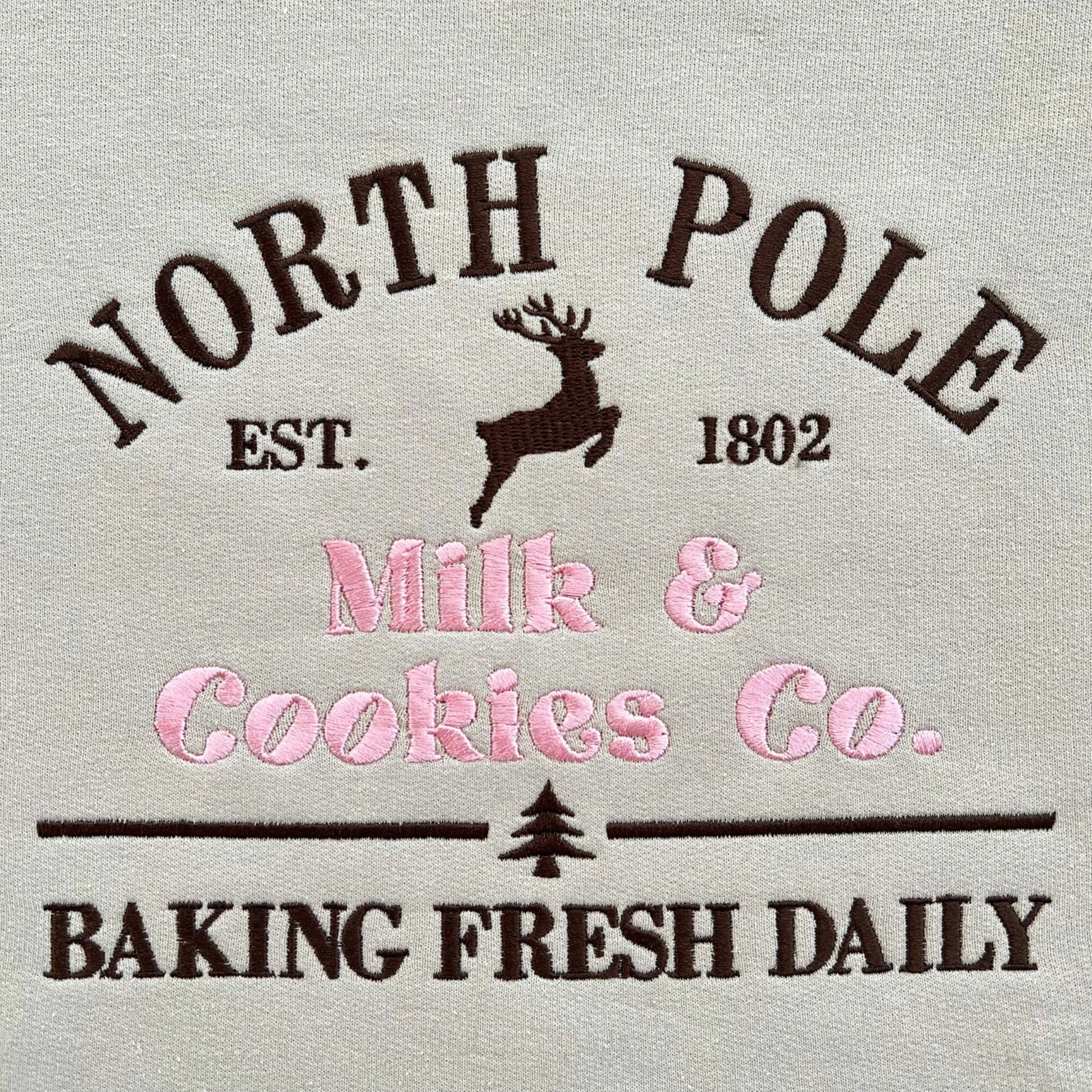 Straight-on close-up of NORTH POLE EST. 1802 with a leaping reindeer above Milk & Cookies Co. in pink