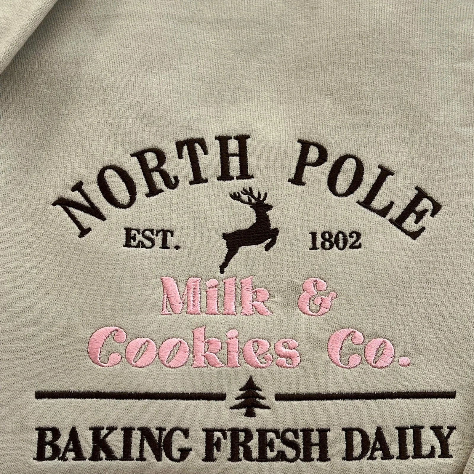 Close-up of the North Pole Milk & Cookies Co. embroidery with a brown reindeer, pink lettering and a small tree