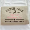 Folded sand sweatshirt with NORTH POLE in brown, a reindeer, EST. 1802 and Milk & Cookies Co. in pink