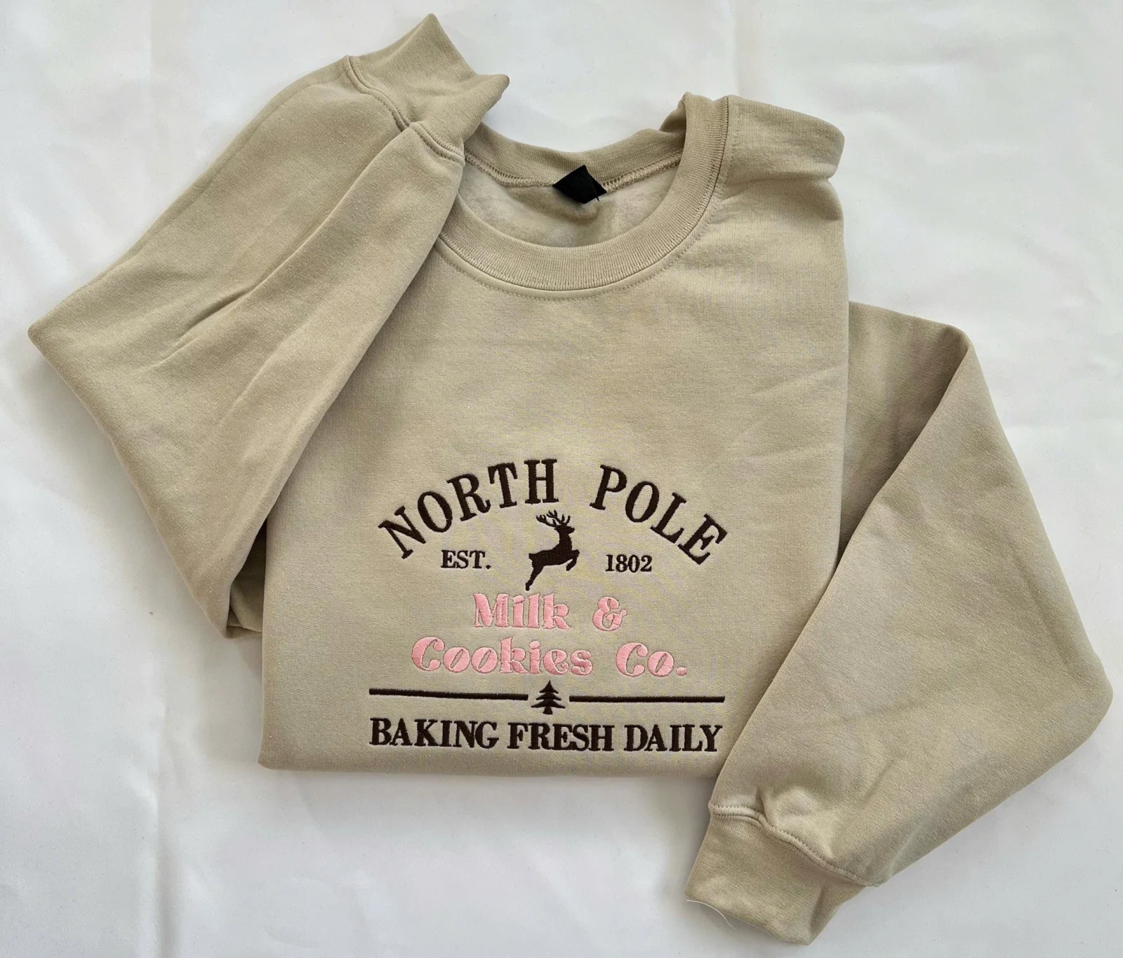 Sand sweatshirt with a North Pole Milk & Cookies Co. bakery sign design, leaping reindeer and Baking Fresh Daily