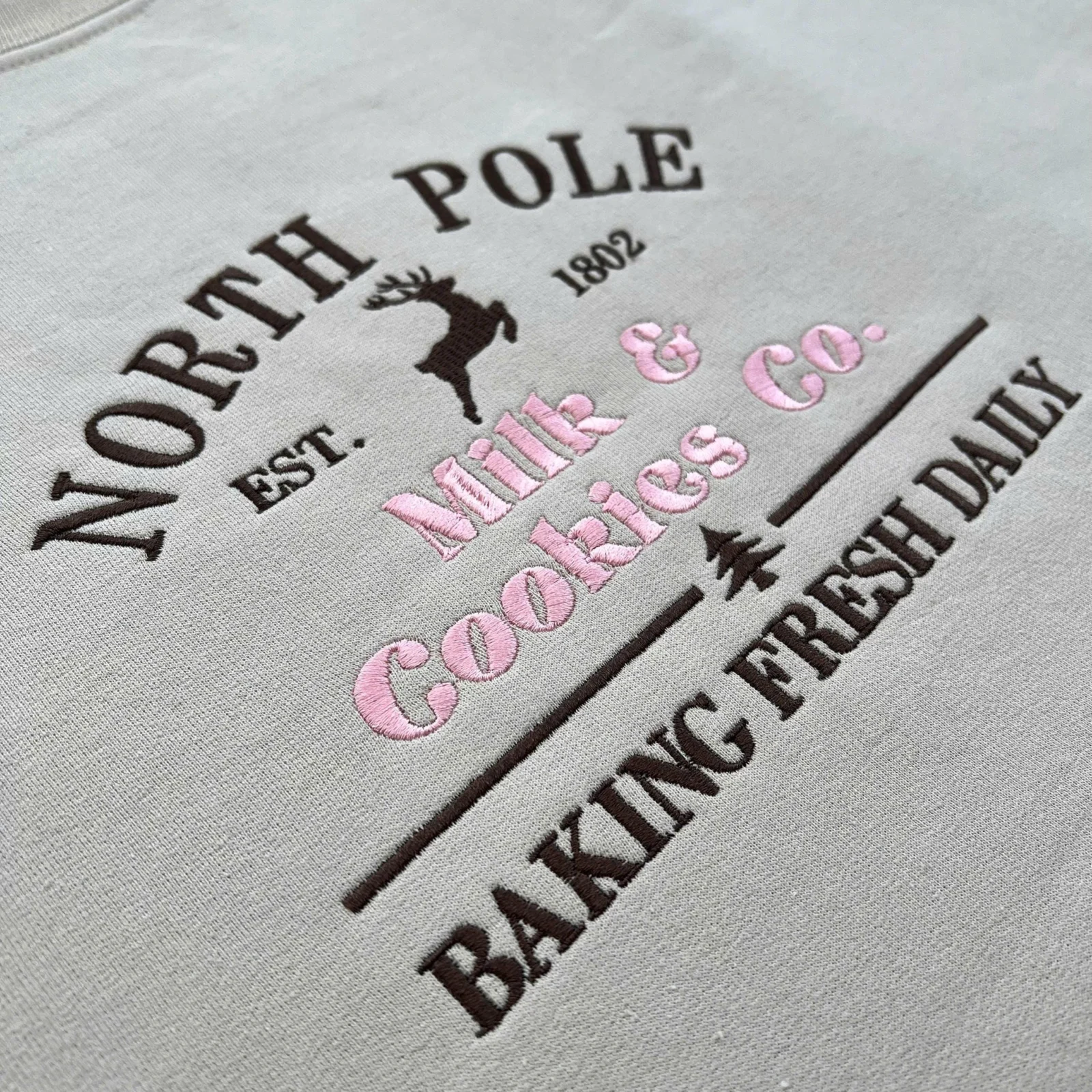 Angled view of brown NORTH POLE lettering, a leaping reindeer, pink Milk & Cookies Co. and BAKING FRESH DAILY