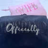 Black hoodie with HUSBAND in tone-on-tone black capitals and Officially in light grey script, pink hoodie behind