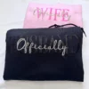 Black HUSBAND hoodie in front of a pink WIFE hoodie, both with layered Officially script embroidery