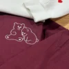 Close-up of a white two-bear outline on maroon fleece and a sleeve initial C beside a red satin heart