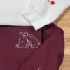 White and maroon crewnecks on a wooden floor with cuddling bear outlines and C with a red heart on the sleeves