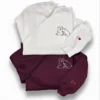 White sweatshirt on top of a maroon one, both with a hugging bears outline on the chest and a heart on the sleeve